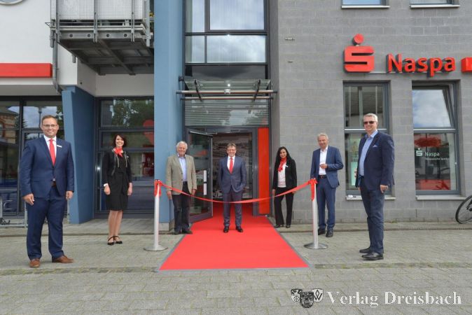 Direktor Stephan Kietzmann, Stefanie van den Breul (ab 1. August Leiterin des Private Banking-Centers), Naspa-Verwaltungsratsmitglied Harald Schindler, Naspa-Vorstandsmitglied Michael Baumann, FC-Leiterin Karima Khabbach, Landrat Michael Cyriax und Hochheims Bürgermeister Dirk Westedt (v.l.n.r.) vor dem Eingang der modernisierten Naspa-Filiale in Hochheim.