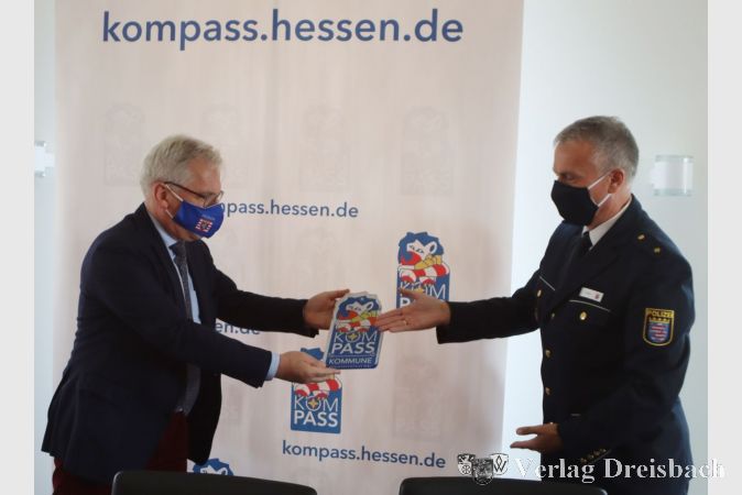 Ein Schild für das Rathaus: Bürgermeister Bernd Blisch (l.) nimmt von Polizist Thomas Trapke ein Schild entgegen, das die Stadt als Teilnehmerkommune am Landesprogramm "KOMPASS" ausweist.