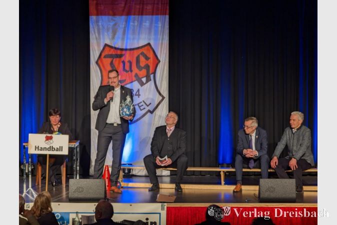 Bürgermeister Christian Seitz (2.v.r.) zählte unter anderem das Engagement der Handballer bei den vielen wiederkehrenden Veranstaltungen in der Gemeinde auf. Links Petra Lehmann am Zeitnehmertisch, rechts auf der Ersatzbank Clemens Weißenberger , der Erste Beigeordnete Franz Jirasek und Landrat Michael Cyriax.