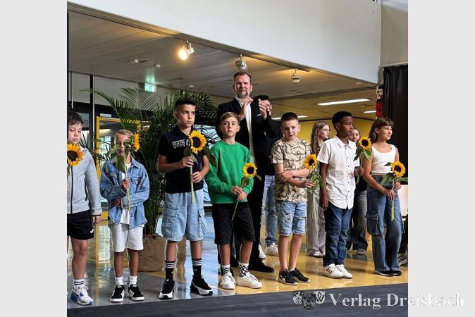 Schulleiter Dr. Christoph Richter inmitten der neuen Schülerinnen und Schüler, die alle eine Sonnenblume erhalten haben.
